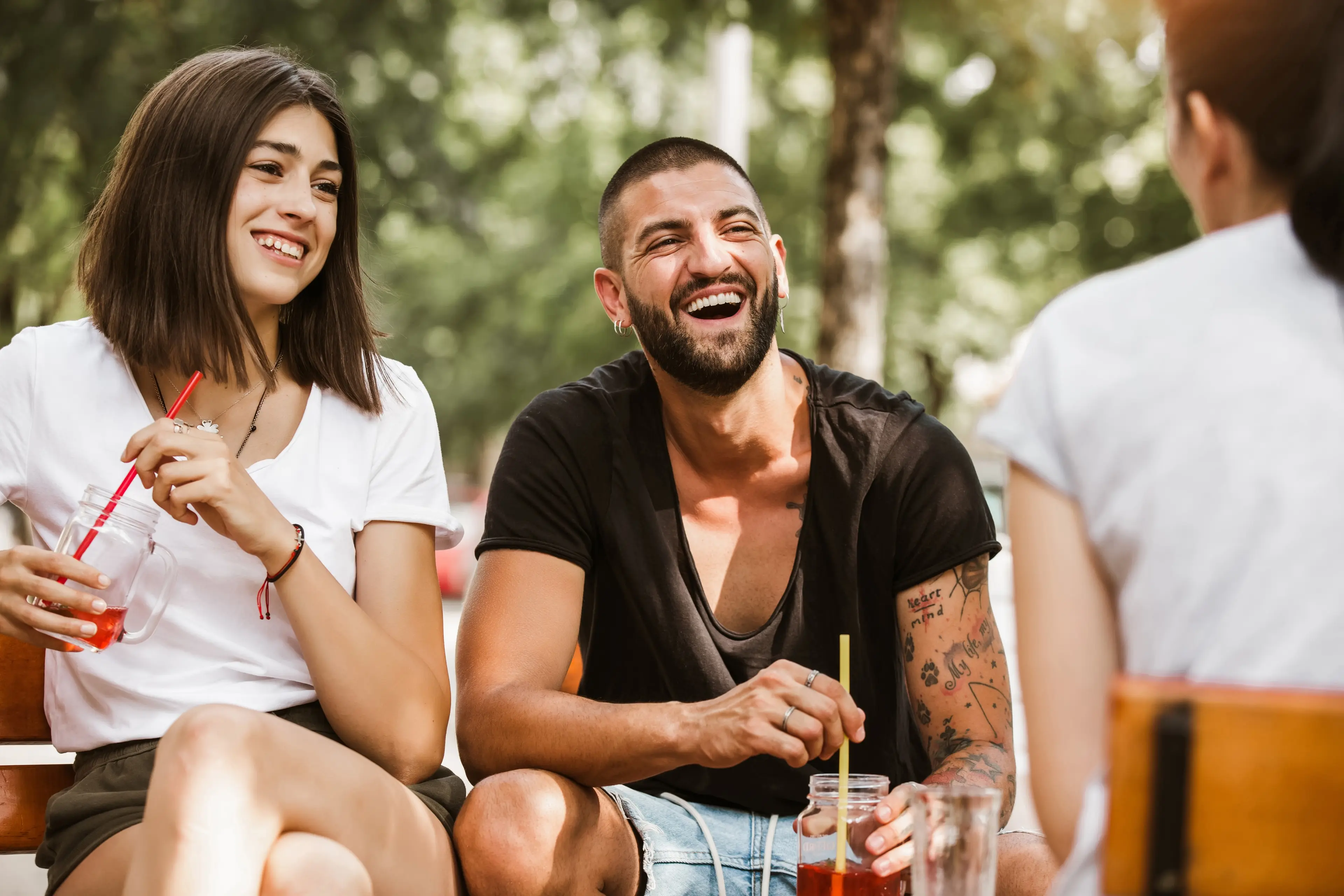 Gruppe junger Freunde sitzt lachend im Freien zusammen und genießt kalte Getränke