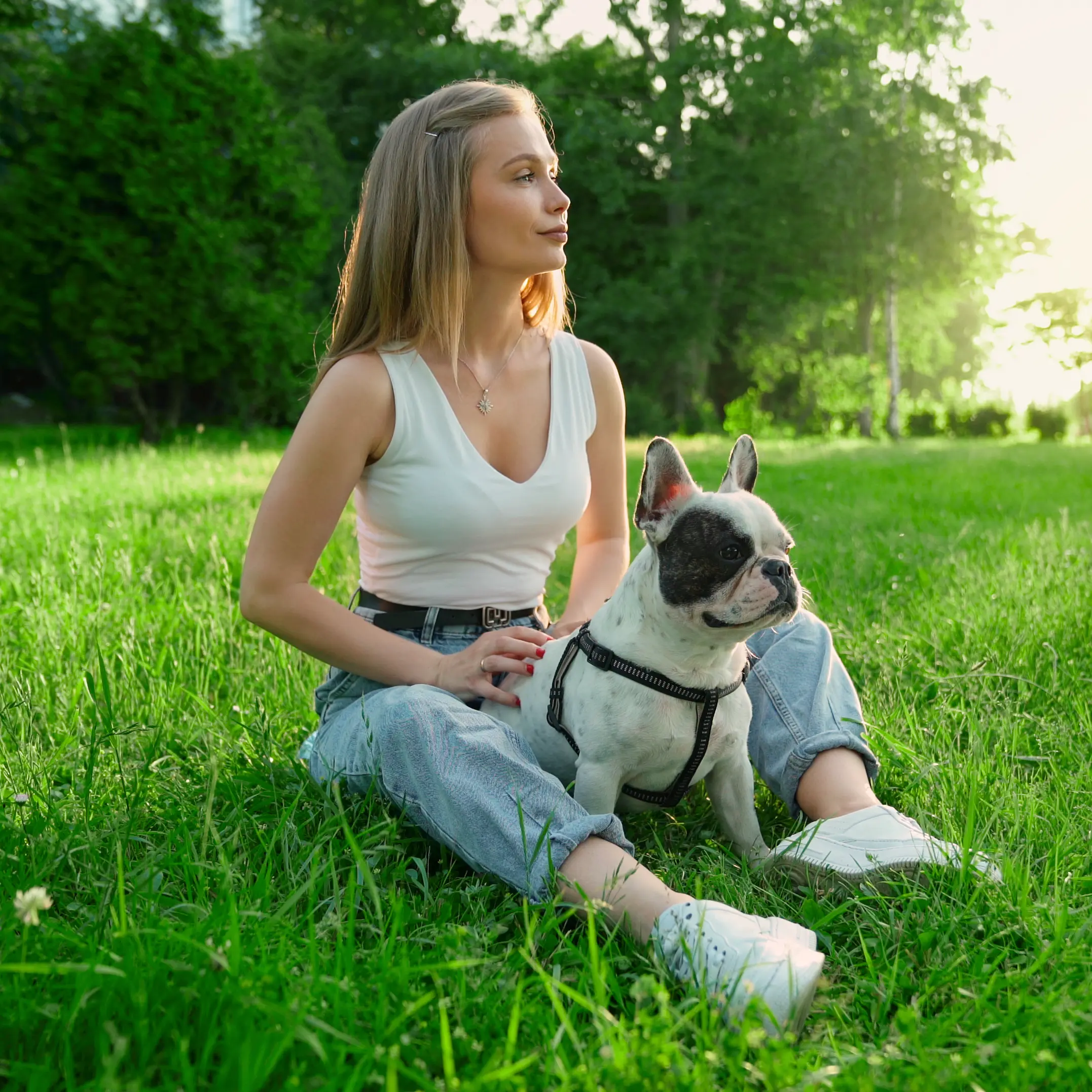 Junge Frau sitzt entspannt mit ihrer französischen Bulldogge auf einer Wiese